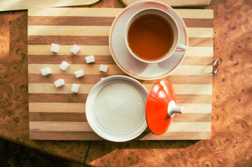 Sugar and refined sugar with a cup of tea in a saucer on the table top view.