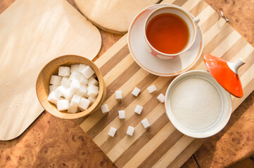 Sugar and refined sugar with a cup of tea in a saucer on the table top view.