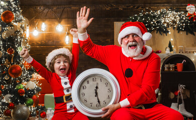 Santa Claus and little helper with clock waving hand and celebration New Year. Christmas time.
