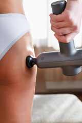 Fototapeta premium Self-massage of the female buttock with a percussion massage gun at home.