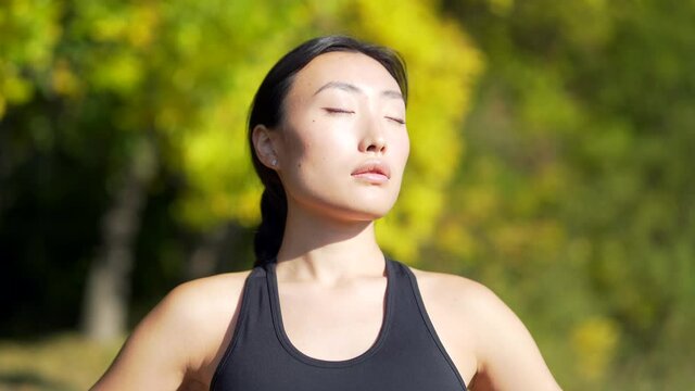 Close up portrait young happy fit asian woman standing in nature between forest trees relaxes, breathes fresh air closing his eyes. Female enjoys a life of peace calm, quiet in park Outdoors Happiness