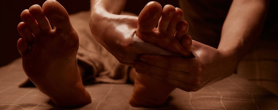 The masseur gives a foot massage to the client. Close-up of hands covered with oil. Subdued lights in the spa. Horizontal banner for website and social networks