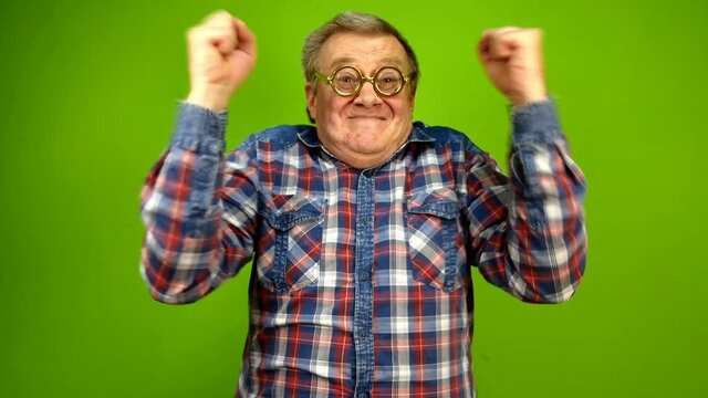 Mature adult strange man in stupid glasses is emotionally happy about something, raise your hands and shakes them with delight. Green screen.