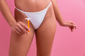 Closeup of a girl in white panties holding a yellow razor blade in her hands on a pink background.