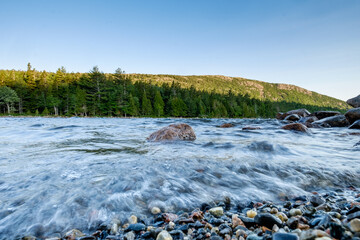 Granite boulders and smaller broken up and smoothed rocks line the shoreline of Jordan Pond in Maine during a windy and rough water day - Powered by Adobe