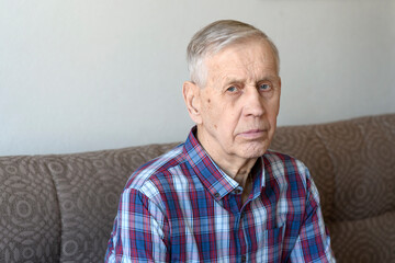 Portrait of an old man. A sad, pensive elderly man sits on the sofa at home. 