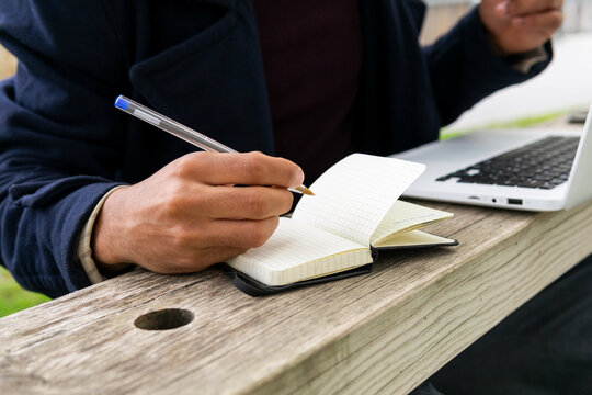 Anonymous black man writing in notepad during remote studies