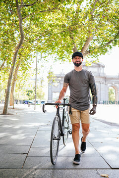 Happy man with artificial arm walking with bike on the street road