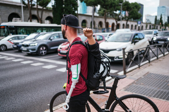 Man with artificial arm standing with bike near road