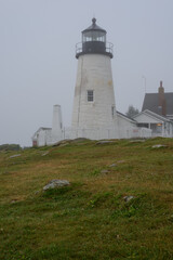 Fototapeta na wymiar The old Pemaquid Lighthouse enveloped in heavy fog sits on the edge of the Atlantic Ocean on the Maine Coast early morning