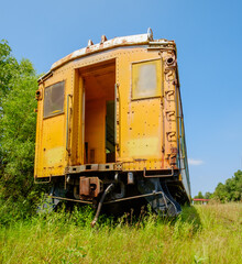 Fototapeta na wymiar Abandoned yellow passenger car sitting in an old train graveyard