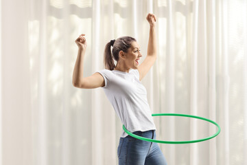 Young woman spinning hula hoop at home with a curtain in the background