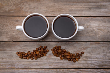 Top view of two cups of coffee and coffee beans in a shape of mustache on wooden table