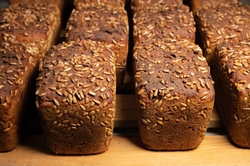 A lot of whole delicious homemade rectangular rye bread with sunflower seeds on top lies on a wooden rack background