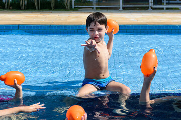 8 year old child sitting at the edge of the pool and ready to throw a water bomb on other children.