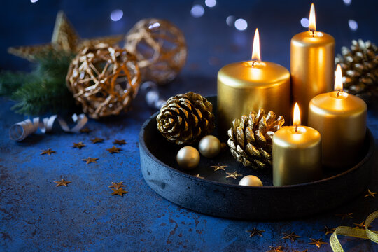 Christmas greeting card with lit golden candles, pine cones festive decorations against dark blue shabby background