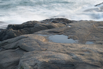 A calm tidal pool sits on granite rocks amidst the rough and crashing surf of the Atlantic Ocean in York Maine