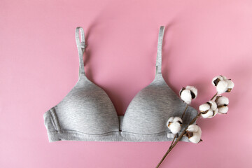 Gray organic or recycled cotton bra with cotton branch on pastel pink background, top view, copy space, flat lay. Concept femininity, comfort, home clothes, underwear, natural textile, minimal style