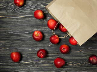 Red apples with a paper bag on a black wooden background.