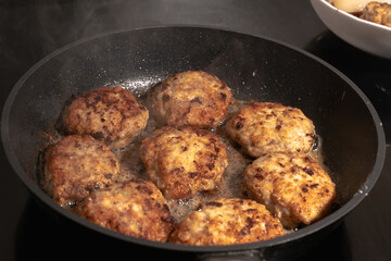 Cooking cutlets in a frying pan on an induction hob. White steam is hovering over hot cutlets in a...