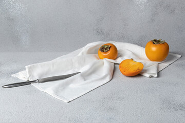 Still life with persimmon. The fruits are lying on a white towel, next to them is a knife. Gray textured background, horizontal orientation, copy space.
