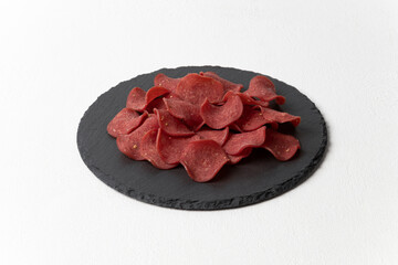 Beer appetizer meat chips on a round black slate board. Horizontal orientation, white textured background, close-up.