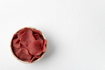 Pork meat chips lying in a ceramic bowl. Top view, copy space, white textured background, horizontal orientation.