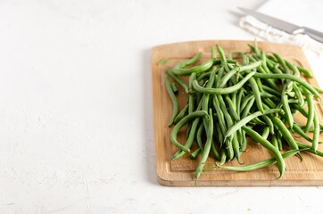 Green beans on a wooden board with a knife and a white napkin, on a white background. 