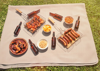 Picnic with grilled chicken wings, grilled sausages, beer bottles and beer snacks in sunny day.