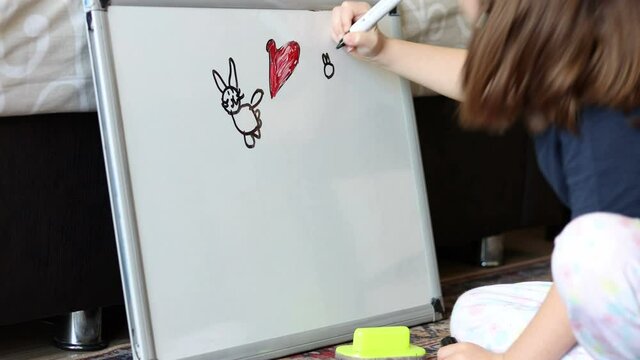 Girl child draws cat pictures with board marker pencil at home
