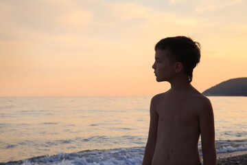 Profile of a boy against the backdrop of a seascape with mountains in the setting sun.