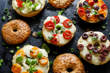 Grilled bagels  with with cherry tomatoes, olives, mozzarella cheese and herbs on a dark...