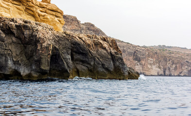 Rocky edges of the Wied iż-Żurrieq inlet near Blue Grotto, Malta, sticking out from Mediterranean Sea and lit by the morning sun. Rock formations with caves.