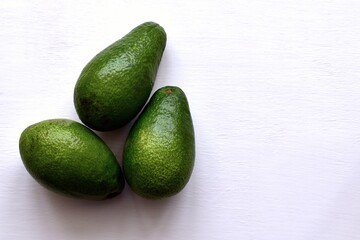 Three ripen green avocados on white table. Top view