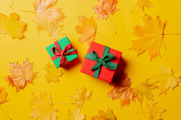 Holiday gift boxes and maple leaves around on yellow background. Top view