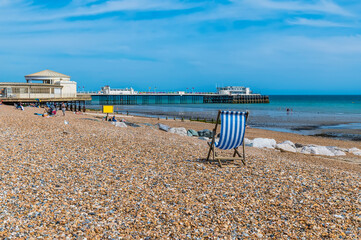 A view past a deck chair along the beach towards the pier at Worthing, Sussex in summertime
