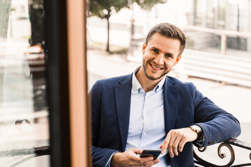 Business is working online using phone. Remote work. Handsome man in cafe on summer terrace.