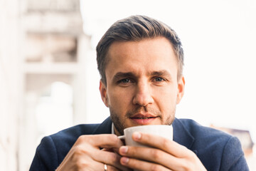 Man like coffee. Handsome man with cup of coffee in cafe. Morning lifestyle of male. Man is sitting on the summer terrace in cafe, drinking coffee and smiling.