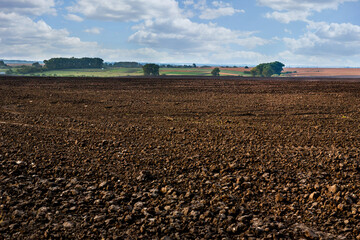 plowed land in the foreground, groves and hills in the background of rural lands