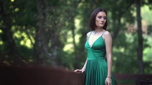 Beautiful young woman in a long green silk dress posing during a photo shooting in the forest.