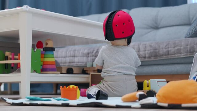 Cute baby boy wearing soft safety helmet discovering new things at home, 7 month old infant on the floor playing, learning to walk, craw sit and stand. High quality 4k footage