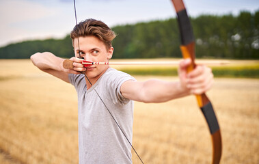 Young male sportsman targeting with traditional bow - Teenager archer practicing archery in nature - Outdoors sports and recreation concept with a millennial boy