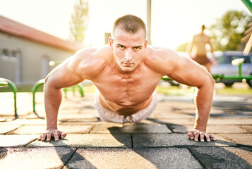 Obraz premium Millennial athletic muscular sportsman doing push ups in a fitness park outdoors - Focused male doing workout on the floor - Strength and bodybuilding concept