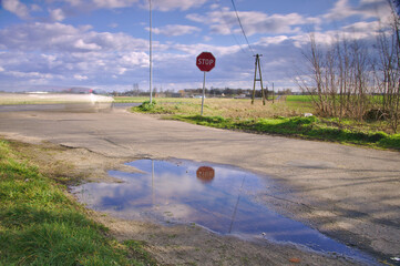 Znak STOP w odbiciu wody i rozmyty samochód z rozmytymi chmurami.