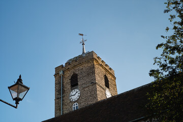 St Peters Church tower and clock  lit by sunlight with a vintage street lamp in the foreground in...