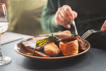 Shallow focus on  yorkshire pudding as part of a meal of roast beef and vegetables. A mans hands...