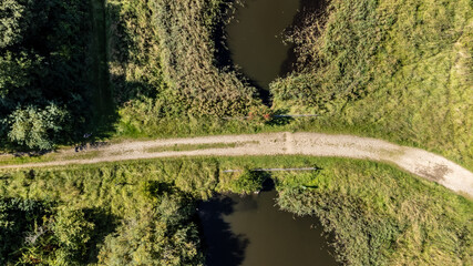 Luftaufnahme von einem Waldweg in der Natur der über einen kleinen Fluss im Wald führt. 