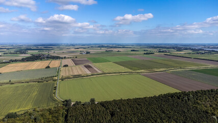 Fototapeta premium Luftaufnahme von flachem Land mit vielen Feldern und Wald bei blauem Himmel und Windrädern im Hintergrund