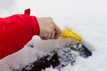 girl cleans car windows from snow with a snow scraper
