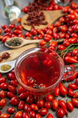 herbal tea cup Dog rose, bunch branch Rosehips, types Rosa canina hips, dry orange peel, tea leaves essential oil and hot on dark background. Medicinal plants and herbs composition